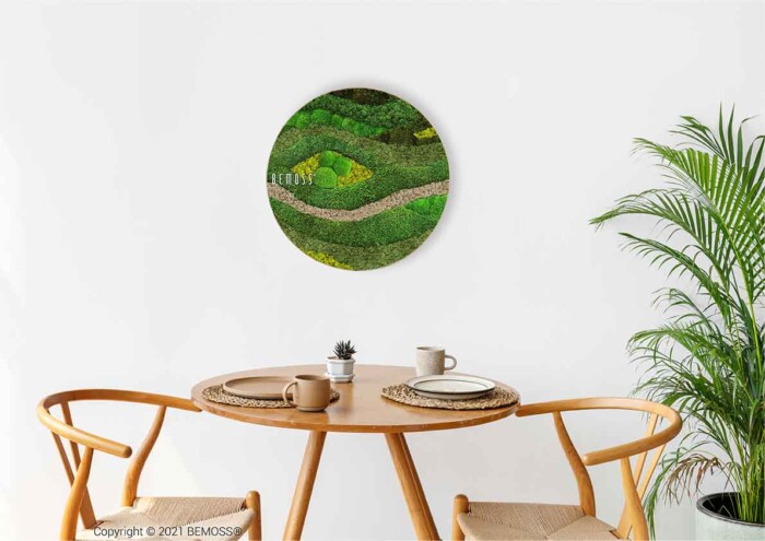 Ein Tisch mit zwei Stühlen und einer Topfpflanze darauf in einem Raum mit einer weißen Wand und einem runden Gemälde, moosbild, mooswand, moos pflanzen, moos, moos deko, moos art