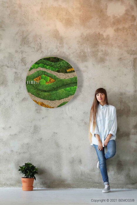 Eine Frau steht vor einer Wand mit einem grünen Gemälde im Gesicht und einem grünen Kreis, moosbild, mooswand, moos pflanzen, moos, moos deko, moos art